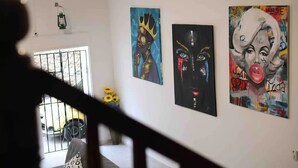 Un corridoio con opere d'arte alle pareti, una finestra con inferriata e una scala.