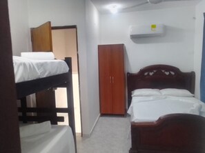 A small, single-room hotel room with a bunk bed, a wardrobe, and an air conditioning unit.