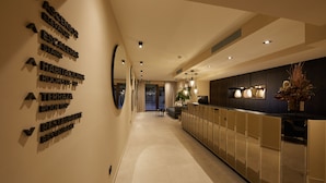 Un pasillo moderno de hotel con indicaciones para las habitaciones, una zona de recepción y vistas al exterior.