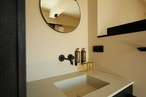 Un baño moderno con un lavabo blanco, un espejo redondo y dos botellas de jabón líquido.