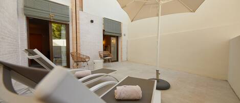 A sunlit outdoor seating area with lounge chairs, a table, and a large umbrella.