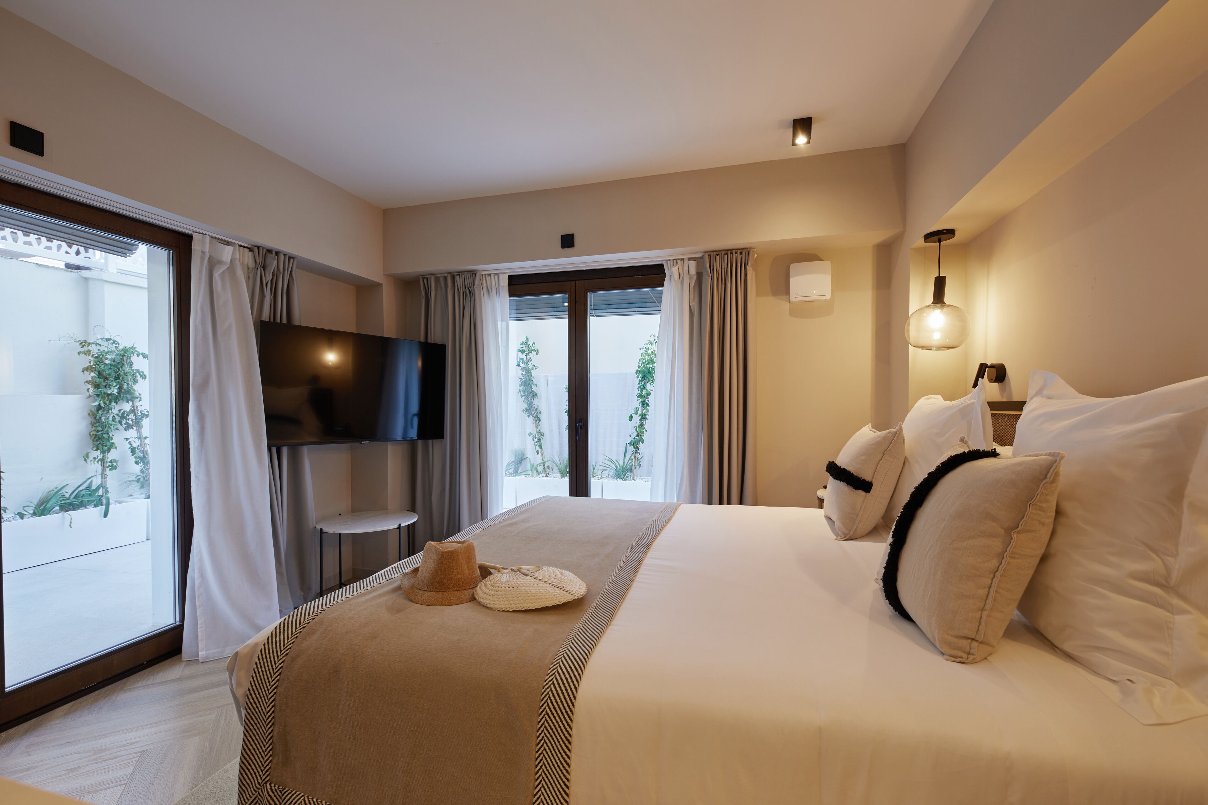 Hotelkamer met een groot bed, een televisie, een balkon met gordijnen en uitzicht op groen.