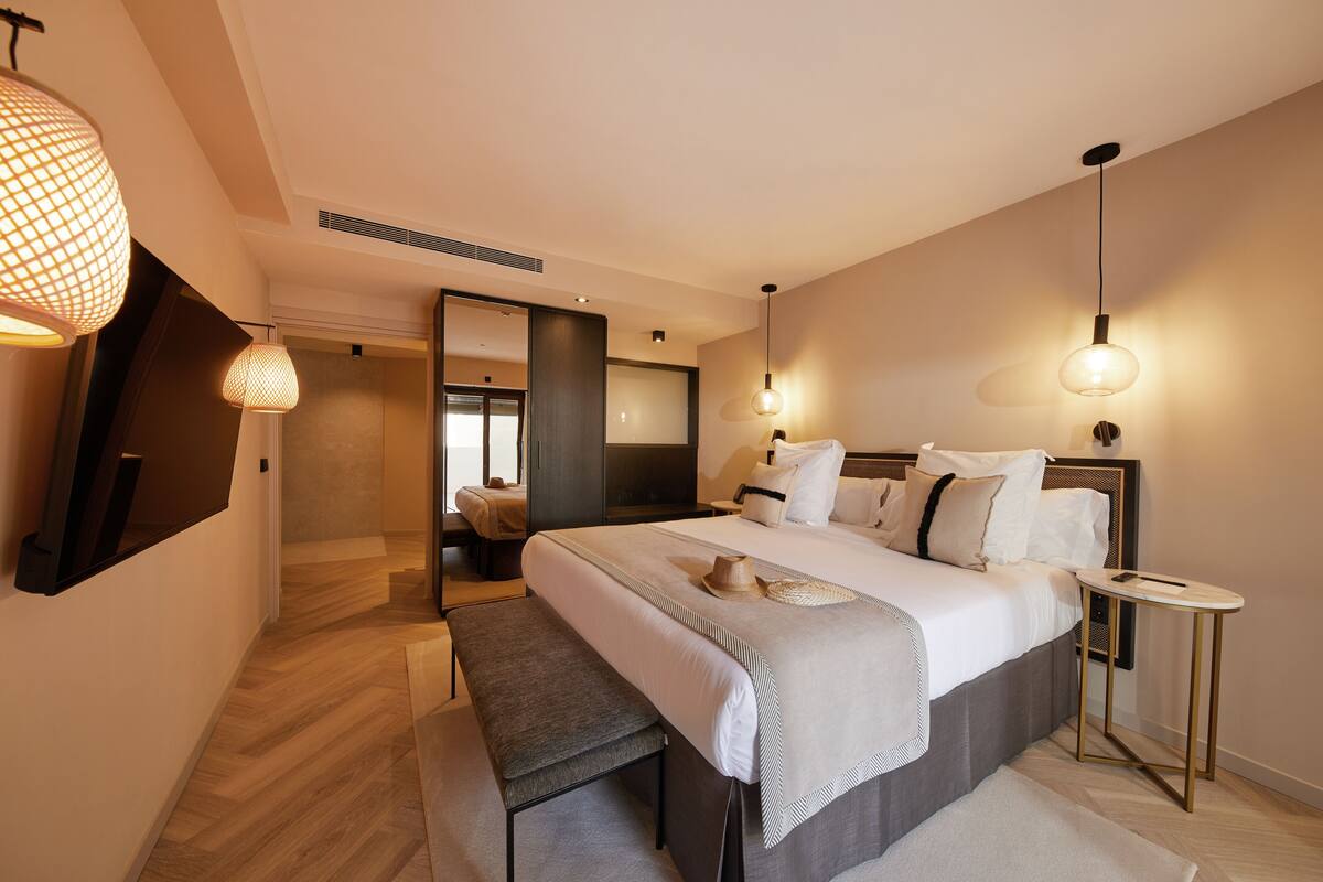 Ein modernes Hotelzimmer mit einem großen Bett, Nachttischen, einer Bank und stimmungsvoller Beleuchtung.