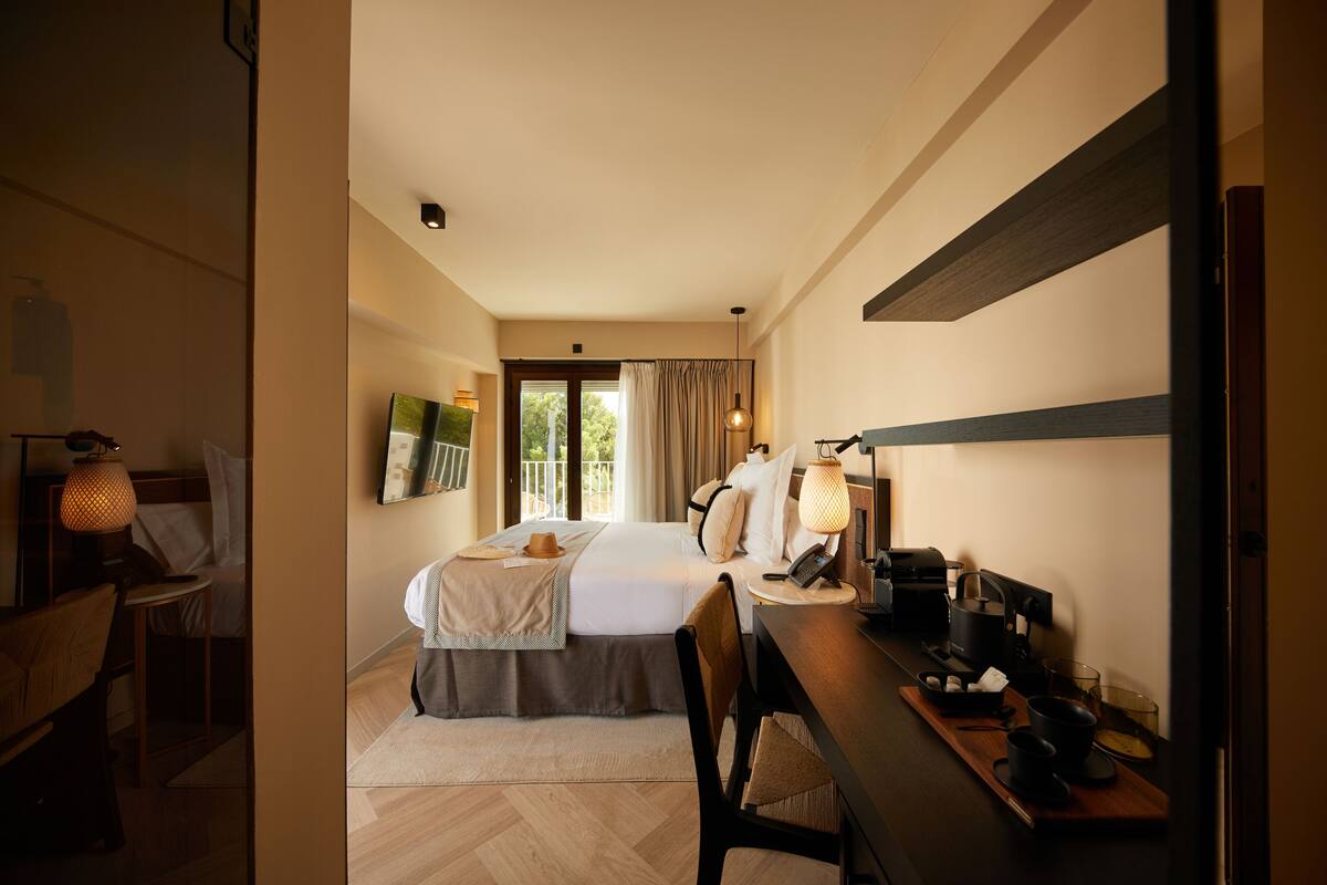 Ein Hotelzimmer mit Bett, Nachttisch, Lampe und Schreibtisch mit Stuhl.