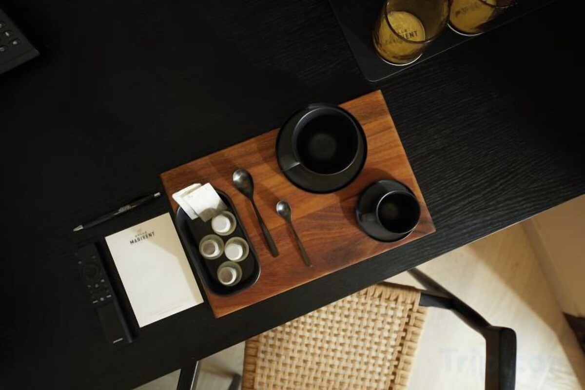 A black table with a wooden tray holding a black cup, a spoon, and a small container with a lid.