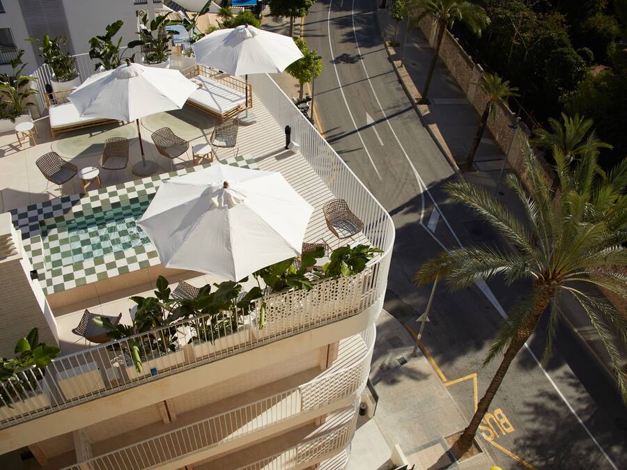 Una terraza en la azotea con piso a cuadros, mobiliario exterior, sombrillas y palmeras.