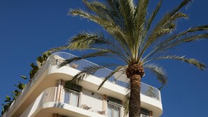 Un hotel de varios pisos con balcones, palmeras y un cielo azul despejado.