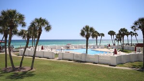 A pool area with lounge chairs and palm trees, overlooking the ocean.