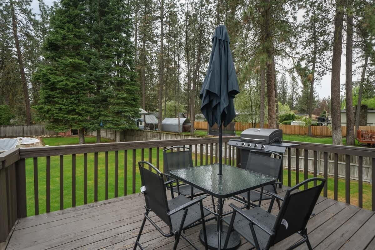 A deck with a glass-top table and chairs, surrounded by a wooden deck and a wooden fence.