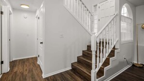 Una escalera con barandillas blancas y peldaños de madera que lleva a un rellano con una puerta blanca.