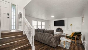 Un salón espacioso con escalera, chimenea y televisor montado en la pared.