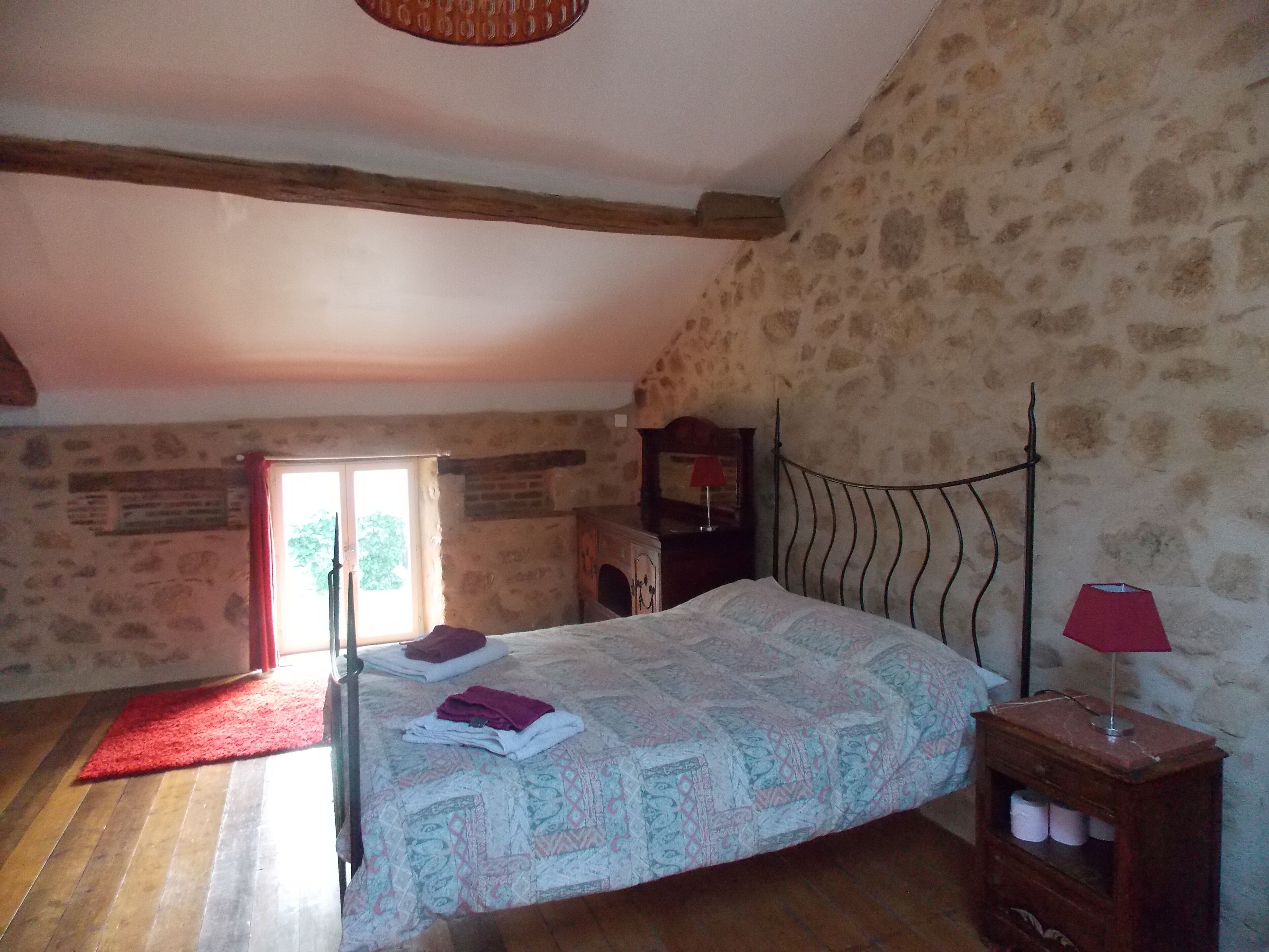 Een slaapkamer met een schuine kap, een houten bedframe, een rood tapijt en een stenen muur.