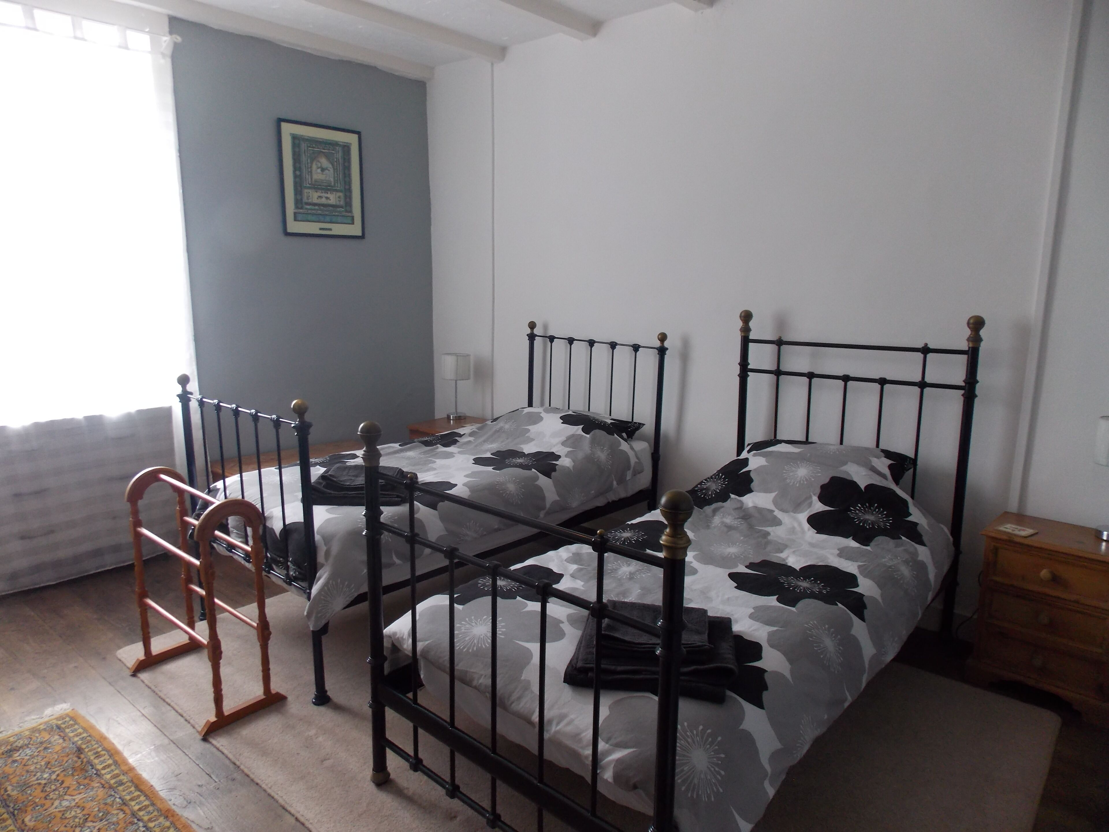 A bedroom with two twin beds, a wooden ladder, a nightstand, and a framed picture on the wall.