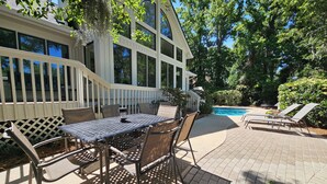 An outdoor patio with a table and chairs, a pool, and a covered area with a railing. - Pet Friendly Golf Course Home w/ Private Pool (Hilton Head Island)