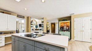 A spacious kitchen with a central island, white cabinetry, and a 'GATHER' sign above the cabinets. - Pet Friendly Golf Course Home w/ Private Pool (Hilton Head Island)