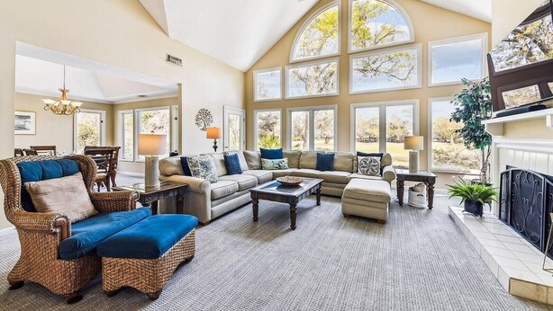 A spacious living room with a high ceiling, large windows, and a fireplace. - Pet Friendly Golf Course Home w/ Private Pool (Hilton Head Island)