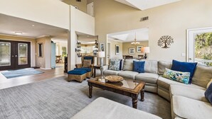 A spacious living room with a high ceiling, a large sofa set, a coffee table, and a dining area visible in the background. - Pet Friendly Golf Course Home w/ Private Pool (Hilton Head Island)