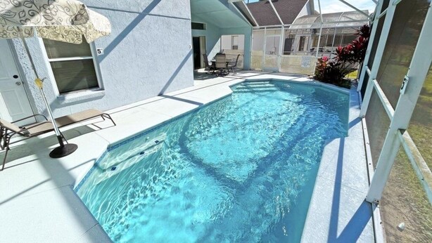 Ein Schwimmbecken mit Glasveranda, eine überdachte Terrasse und ein Haus im Hintergrund.