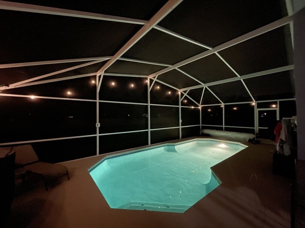A swimming pool with a covered area, surrounded by a white structure with string lights.