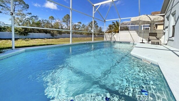 Une piscine à l’eau d’un bleu limpide, entourée d’une clôture blanche et dotée d’un espace abrité avec un toit à motifs.