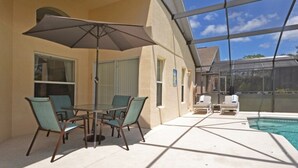 Uma área externa coberta com piscina, mesa e cadeiras, e um grande guarda-sol.