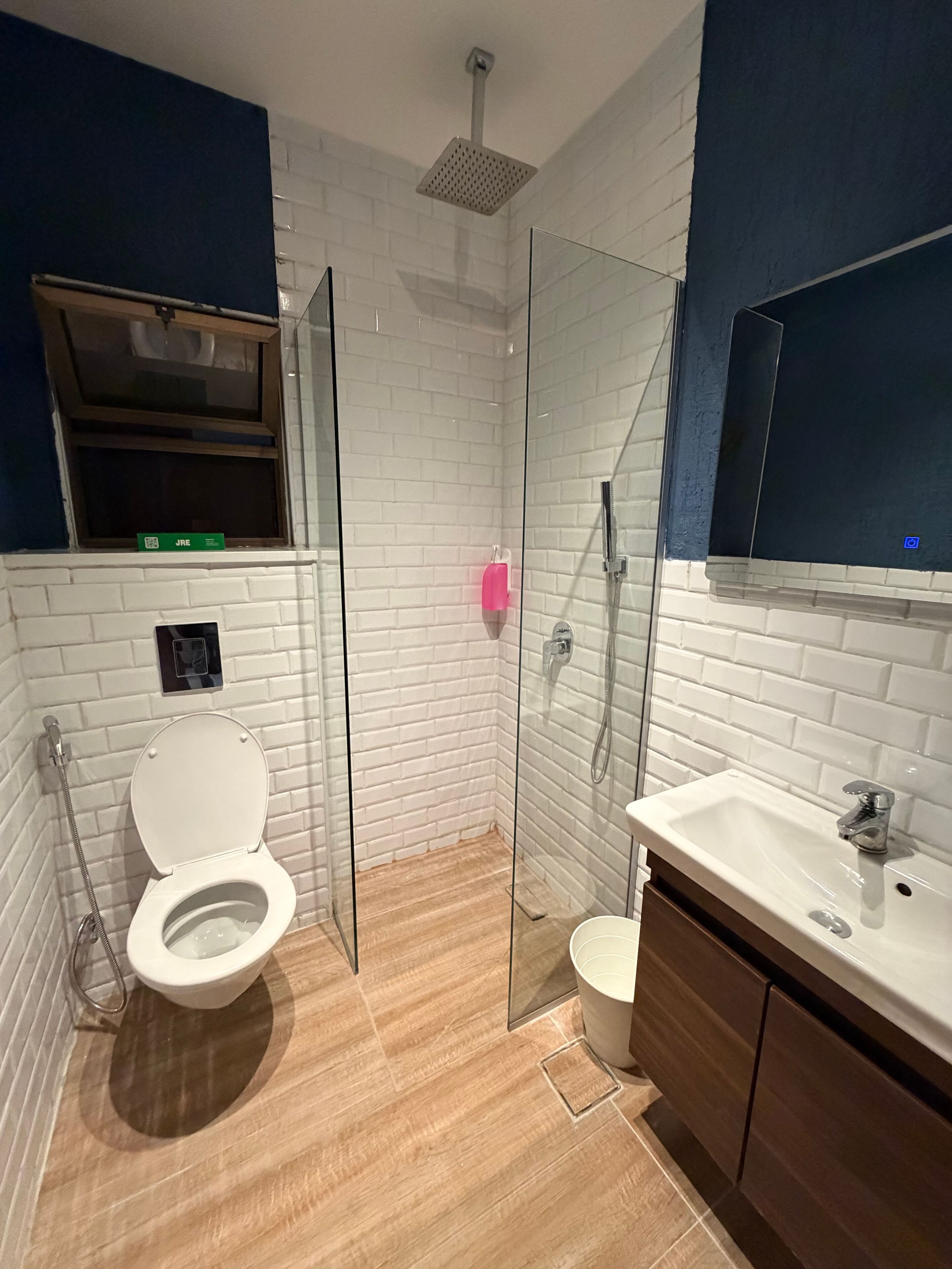 A modern bathroom with a white brick wall, a glass shower enclosure, a white toilet, and a wooden vanity with a sink.