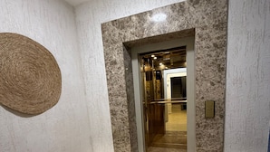 A room with a marble floor, a door with a textured wall, and a woven wall hanging.