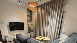 A modern living room with a large flat-screen TV, a grey sofa, a coffee table, and a decorative plant.
