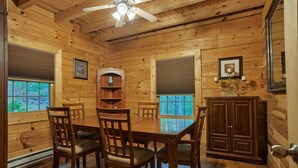 A wooden cabin interior with a dining table, chairs, a ceiling fan, and a cabinet. - Secluded Log Home on 11 Forested Acres🌲🌲🌲 Jacuzzi🔥 Fire Pit🔥 Wood Stove🔥 (Dunmore)