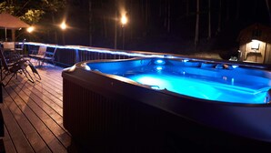 A hot tub on a wooden deck at night with ambient lighting. - Secluded Log Home on 11 Forested Acres🌲🌲🌲 Jacuzzi🔥 Fire Pit🔥 Wood Stove🔥 (Dunmore)