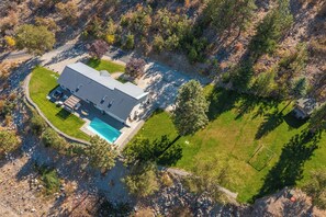 Luchtbeeld van een modern, tweelaags huis met zwembad, omgeven door een verzorgd gazon en bomen.