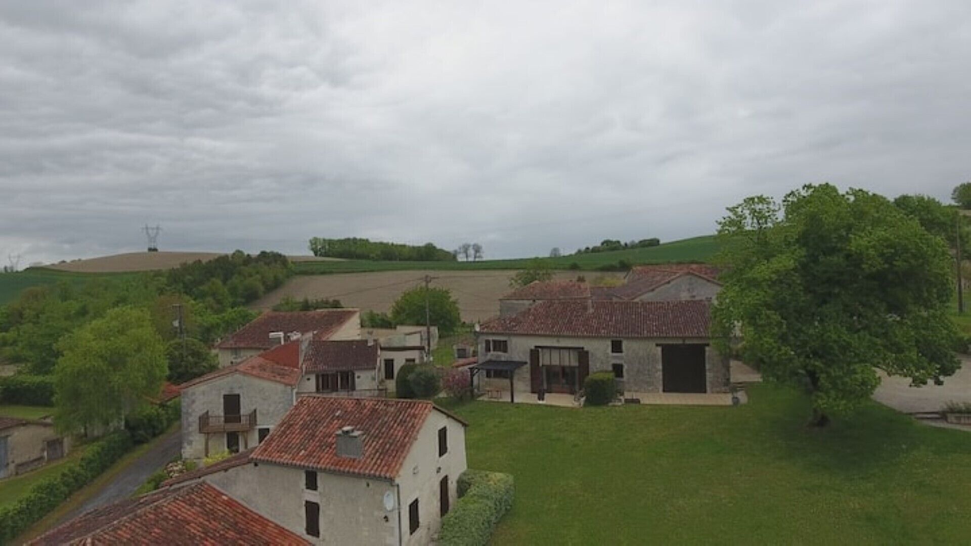 Un village rural avec des bâtiments traditionnels en pierre, un grand champ ouvert et une colline en arrière-plan.