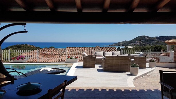 A rooftop terrace with a pool, wicker furniture, and a view of the sea and hills.