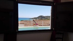 A window view of a pool with a tiled deck and a mountain in the background.