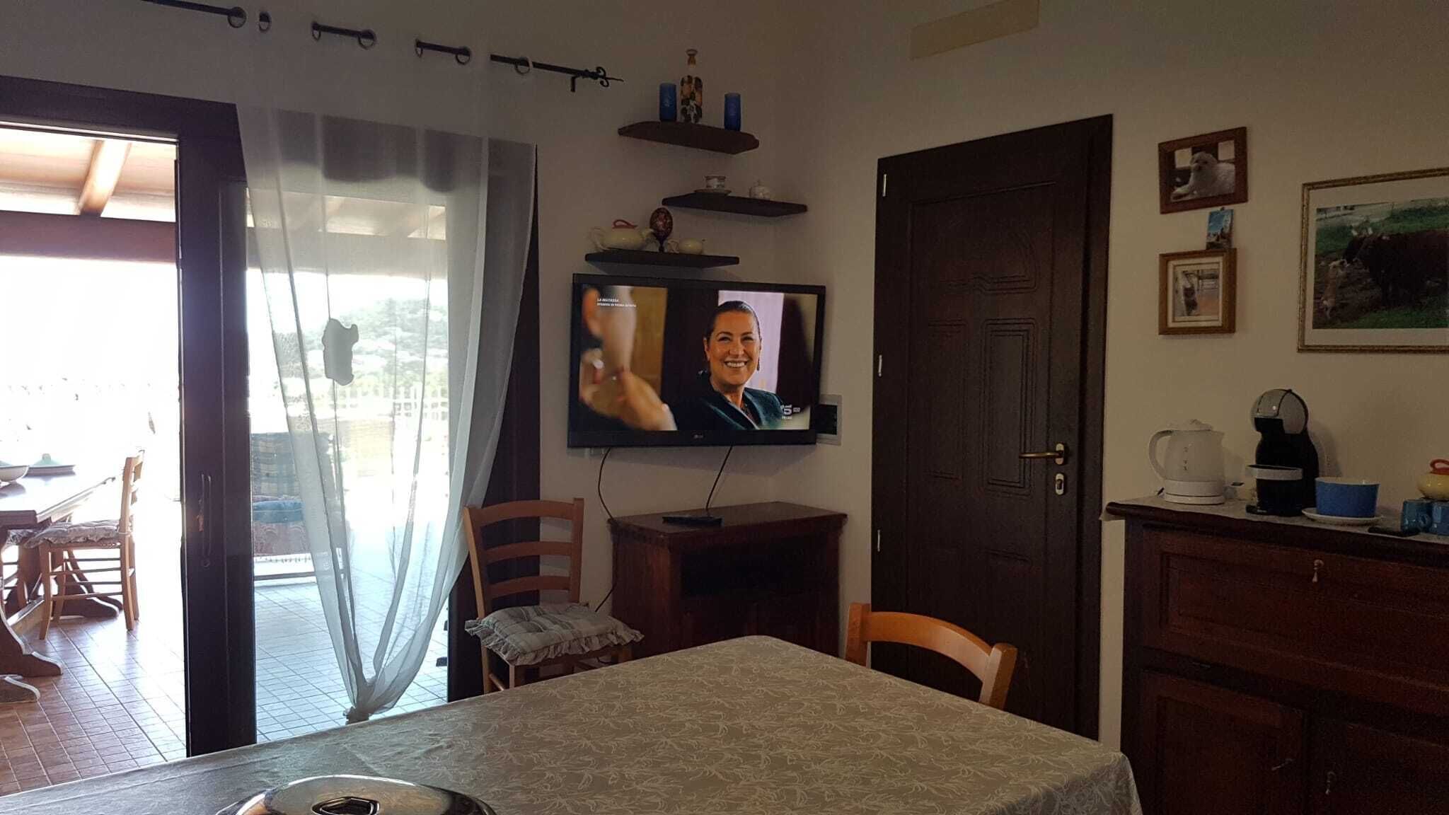 Een eethoek met een tafel, stoelen, een aan de muur bevestigde televisie en een deur.