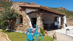 A stone house with a tiled roof, a covered porch, and a bicycle in the foreground.