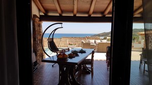 An open patio with a dining table, chairs, and a view of the sea.