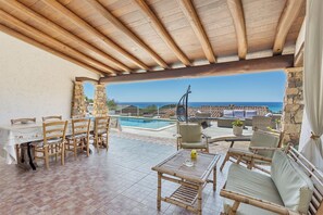 Un patio couvert avec une piscine, des sièges d’extérieur et une vue sur l’océan.