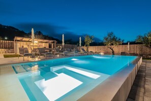 A rectangular swimming pool with a clear blue water feature, surrounded by lounge chairs and a wooden deck. - Claudio Stone House!! (Zakynthos)