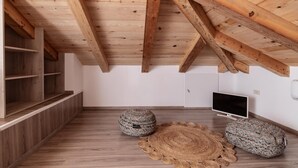 A spacious attic room with wooden beams, a television, and two round woven rugs on the floor. - Claudio Stone House!! (Zakynthos)