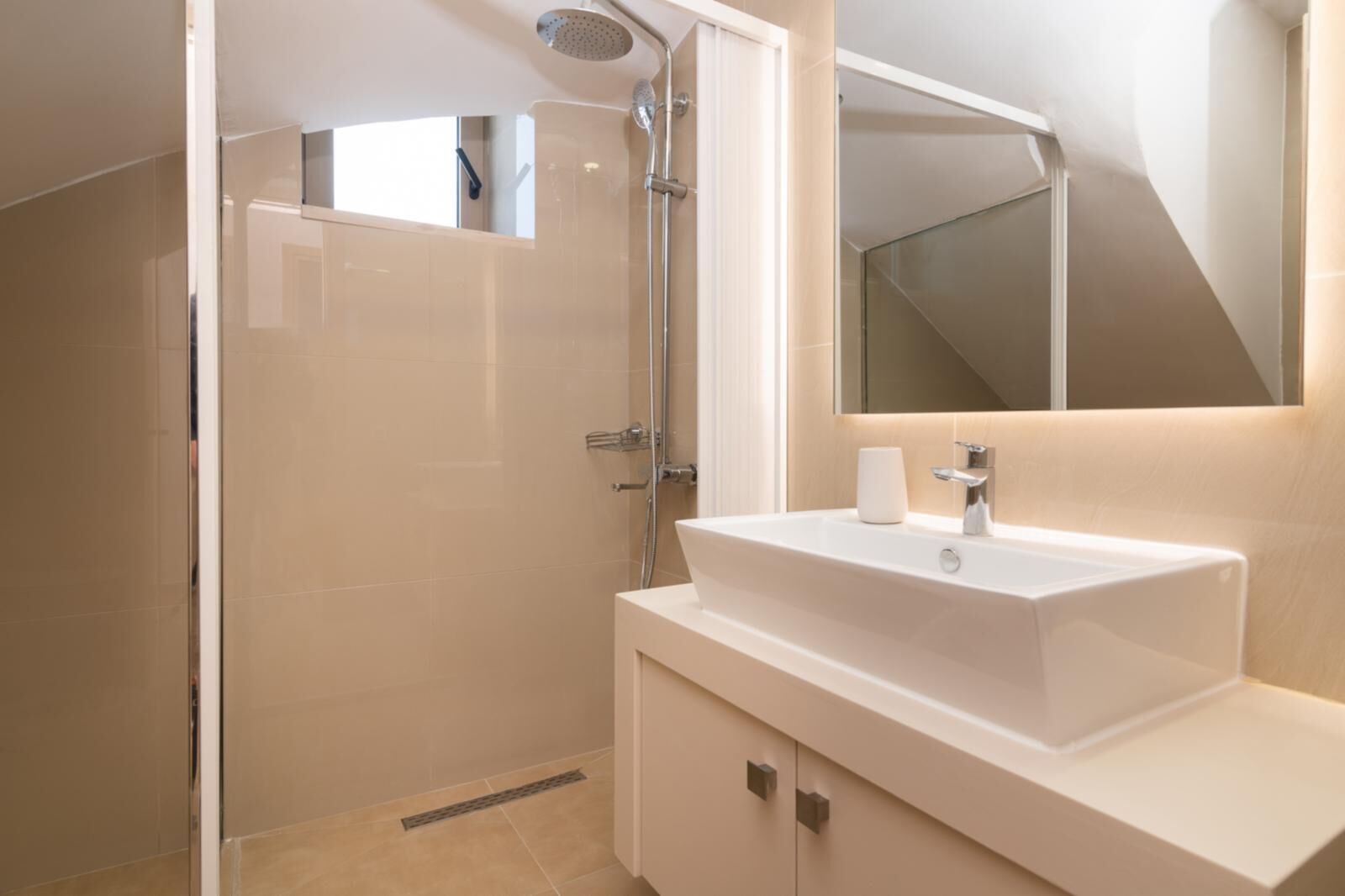 A modern bathroom with a glass-enclosed shower, a white sink with a mirror above, and beige tiles.