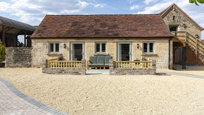 Un bâtiment en pierre avec un toit en tuiles, un porche à l’avant doté d’un banc et un escalier menant à un étage supérieur.