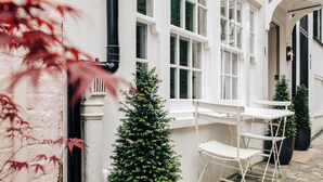 Ein weißes Gebäude mit großen Fenstern, einer kleinen Weihnachtstanne und einem weißen Tisch mit Stuhl im Freien.