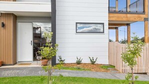 A modern house with a white exterior, a wooden deck, and a small garden with potted plants.