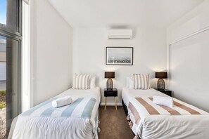 Une chambre d’hôtel avec deux lits, une fenêtre, un climatiseur, un tableau encadré et des lampes de chevet.