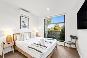Een slaapkamer met een groot bed, bedlampen, een ingelijst kunstwerk, een raam met uitzicht en een stoel.
