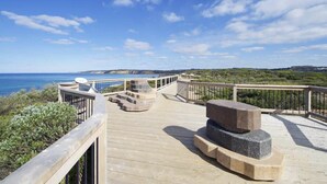 A wooden deck with a stone bench and a satellite dish, overlooking a coastal landscape.