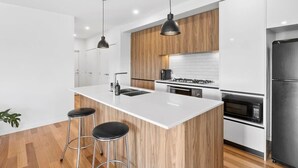 A modern kitchen with a central island, wooden cabinets, stainless steel appliances, and pendant lighting.