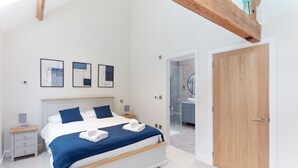 A bedroom with a bed, bedside tables, a wardrobe, and a bathroom visible through an open door. - Luxury 2-Bed Cotswolds Barn with Two Ensuite Kings (Gloucester)