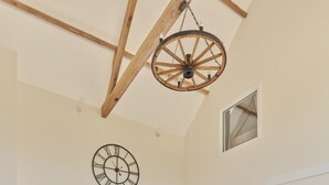 A spacious living room with a blue sectional sofa, a wooden dining table with blue chairs, a large wall clock, and a ceiling fan. - Luxury 2-Bed Cotswolds Barn with Two Ensuite Kings (Gloucester)